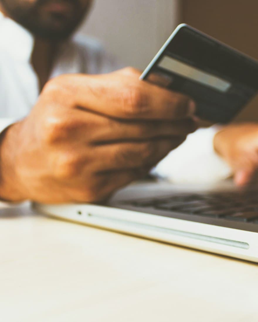 Someone holding a payment card while using a laptop